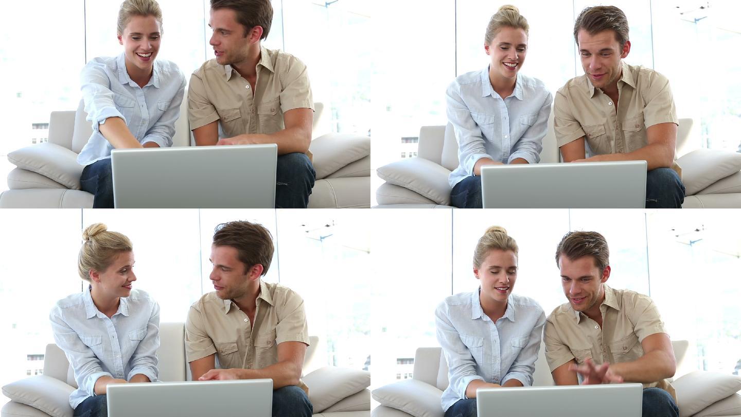 一对夫妇坐在客厅沙发上看笔记本电脑