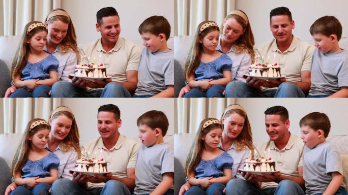 快乐的年轻家庭坐在沙发上庆祝一个生日在家里的客厅