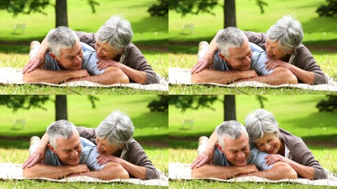 在一个阳光明媚的日子里，一对老年夫妇躺在毛毯上在公园里放松