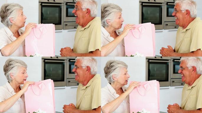 一个老人在厨房里给他的伴侣一个装在粉色袋子里的礼物