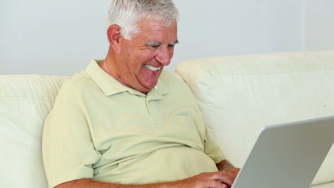老人坐在沙发上使用笔记本电脑，在家里的客厅