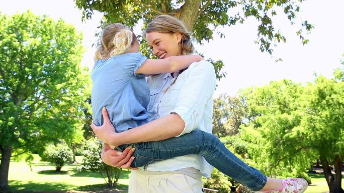 在一个阳光明媚的日子里，快乐的妈妈抱着她的小女儿在公园里