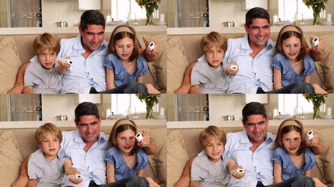 可爱的孩子和他们的父亲在客厅的沙发上玩电子游戏
