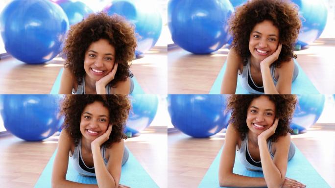 微笑的女人躺在健身房的运动垫子上