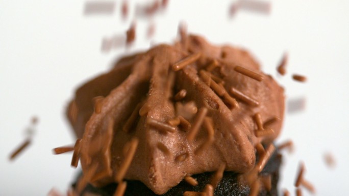 慢镜头中，巧克力屑落在巧克力纸杯蛋糕上