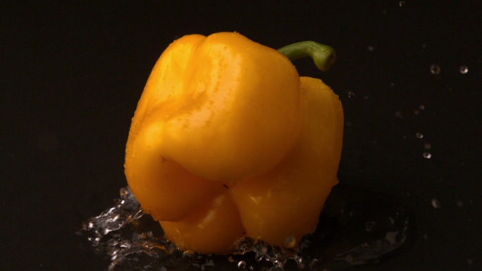 黄色的辣椒以慢镜头落在潮湿的黑色表面