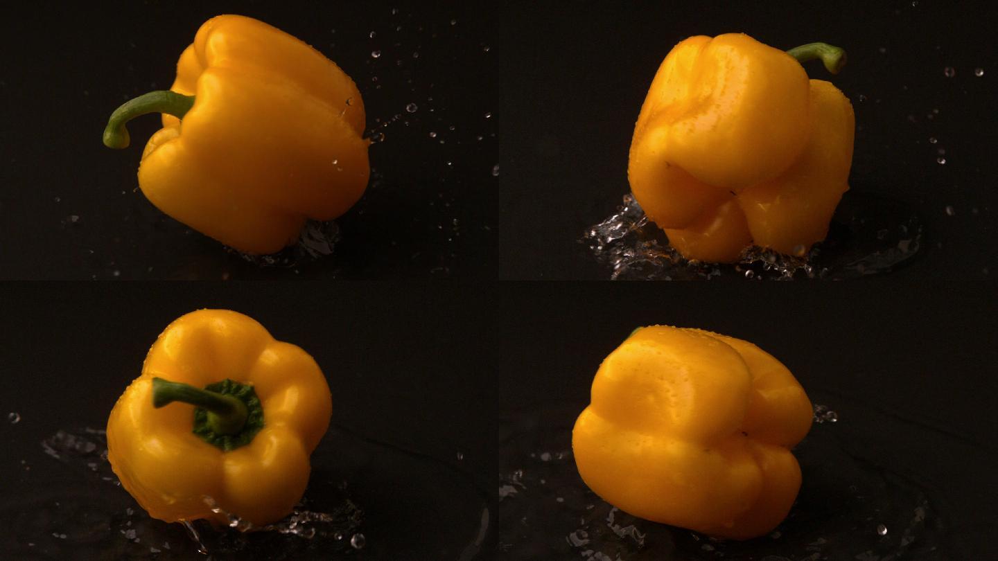 黄色的辣椒以慢镜头落在潮湿的黑色表面