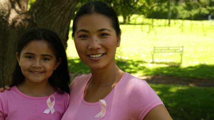 在一个阳光明媚的日子里，母亲和女儿穿着粉红色的衣服在公园里宣传乳腺癌