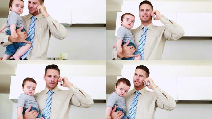 父亲在上班前抱着他的孩子在家里的厨房里打电话