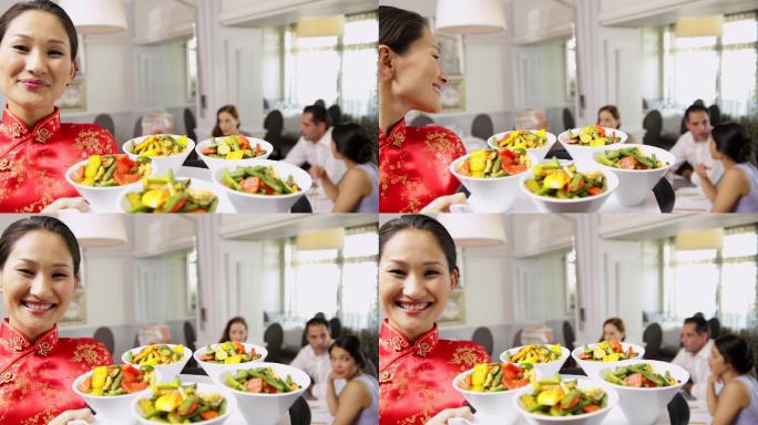 在一家中国餐馆里，微笑的女服务员正在用托盘端着几碗蔬菜