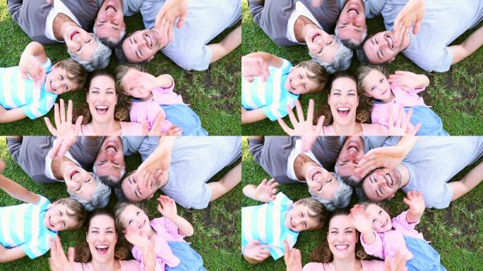 在一个阳光明媚的日子里，一家人躺在公园里对着镜头微笑