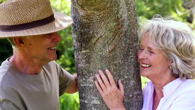 一对退休夫妇在花园里靠在树上互相微笑