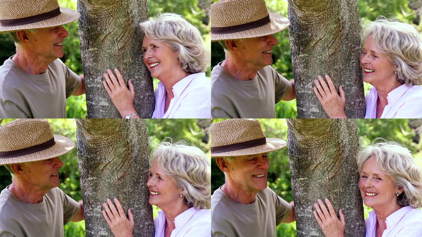 一对退休夫妇在花园里靠在树上互相微笑