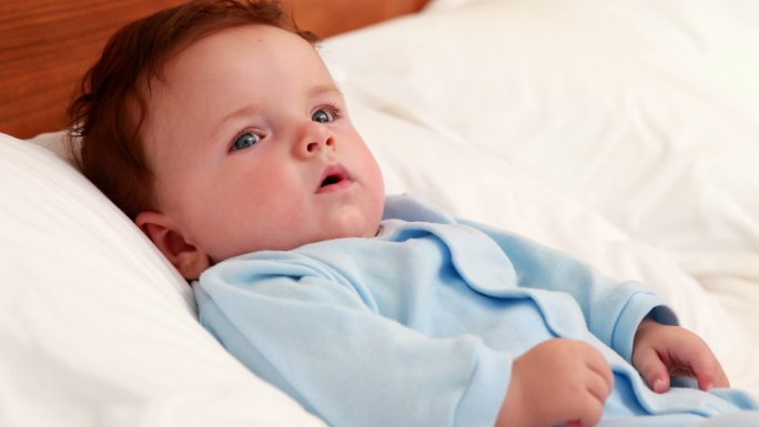 穿蓝色婴儿服的男婴躺在家里卧室的床上