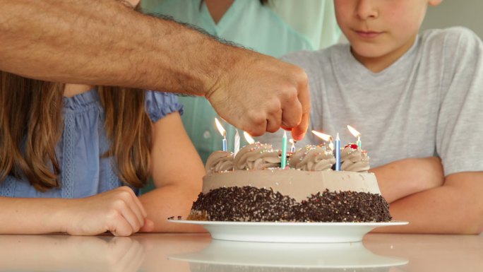 父亲在餐厅为他的家人在生日蛋糕上点燃蜡烛