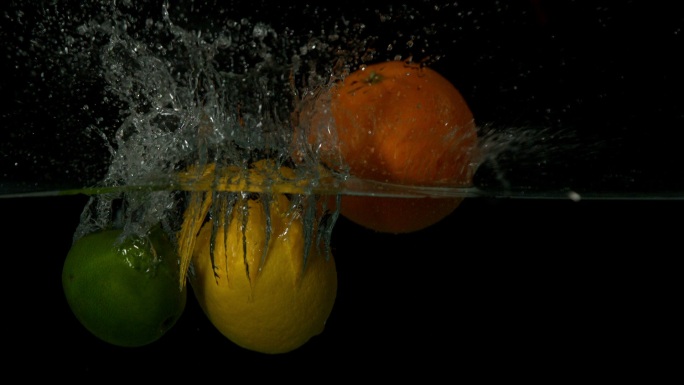 在黑色背景的慢镜头中，柠檬、橙子和酸橙跳入水中