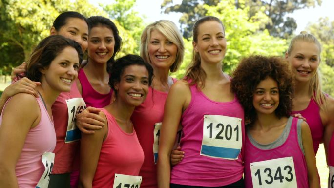 在一个阳光明媚的日子里，一名微笑的女子在公园里为乳腺癌意识进行粉色赛跑