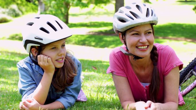 在一个阳光明媚的日子，妈妈和女儿在公园里骑自行车休息
