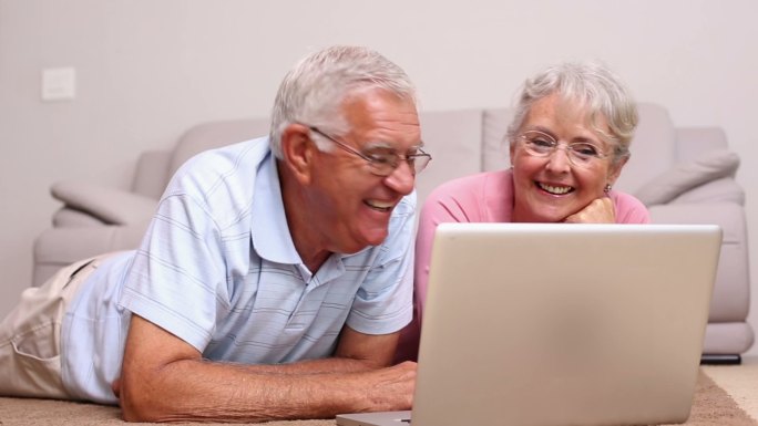 一对老年夫妇躺在客厅地板上使用笔记本电脑