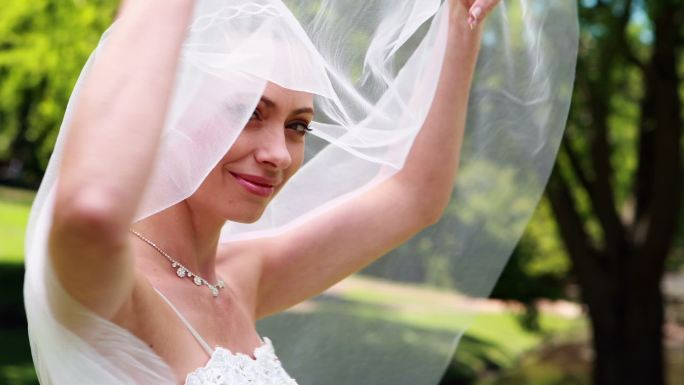 美丽的新娘对着镜头微笑，在她的婚礼上揭开她的面纱
