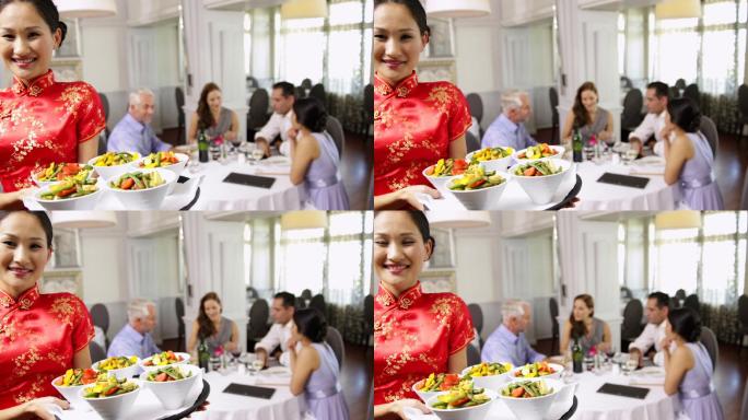 在一家中国餐馆里，快乐的女服务员正在用托盘端着几碗蔬菜