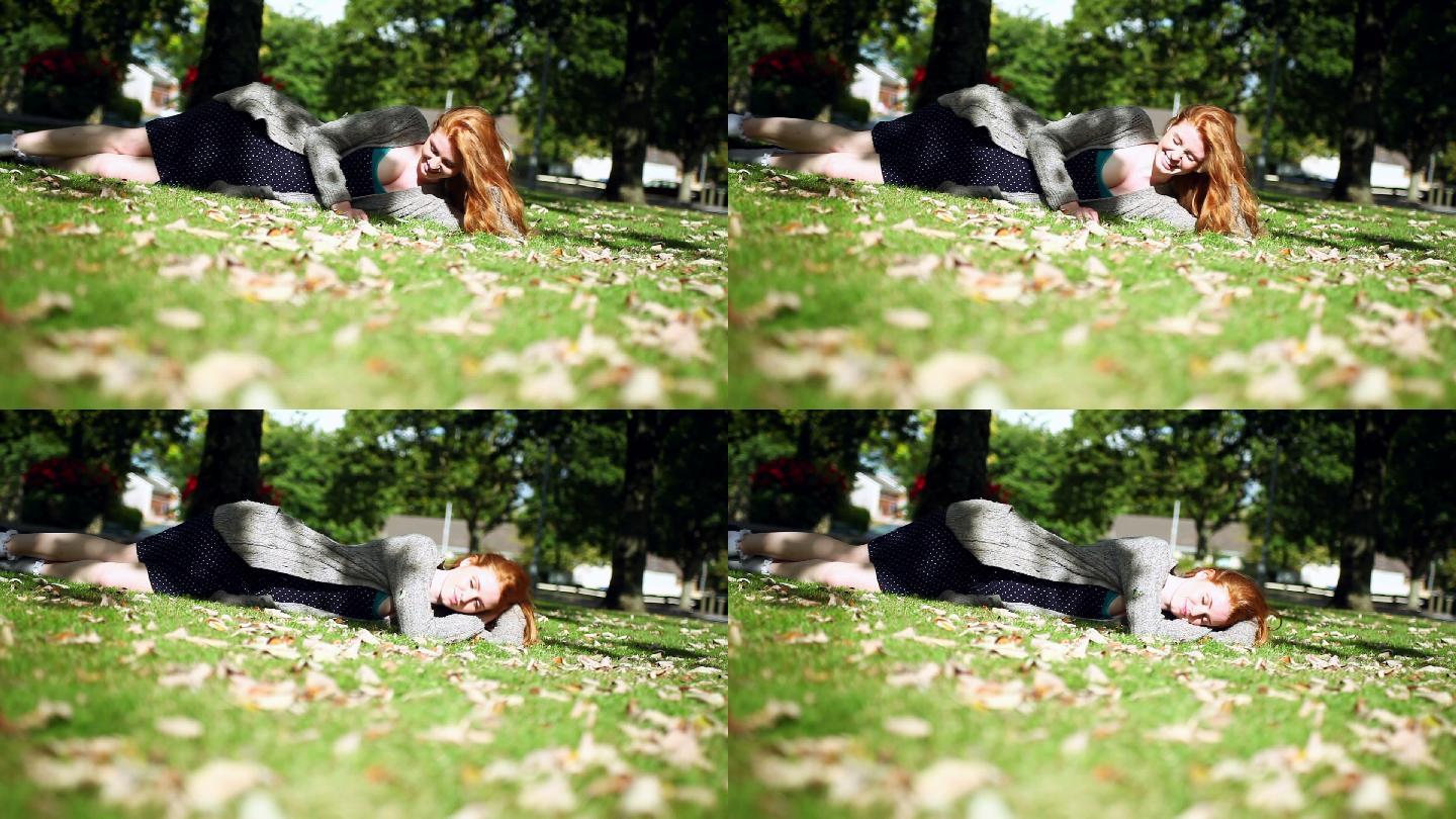 开朗的红发女郎在明亮的阳光下躺在绿色的草坪上放松