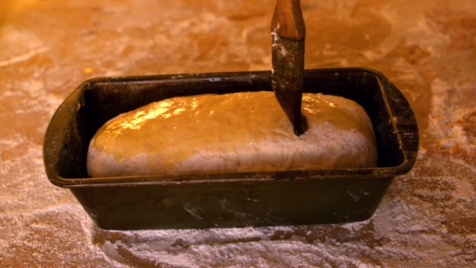 用慢镜头在面粉桌上的面包盒里的生面团上刷橄榄油