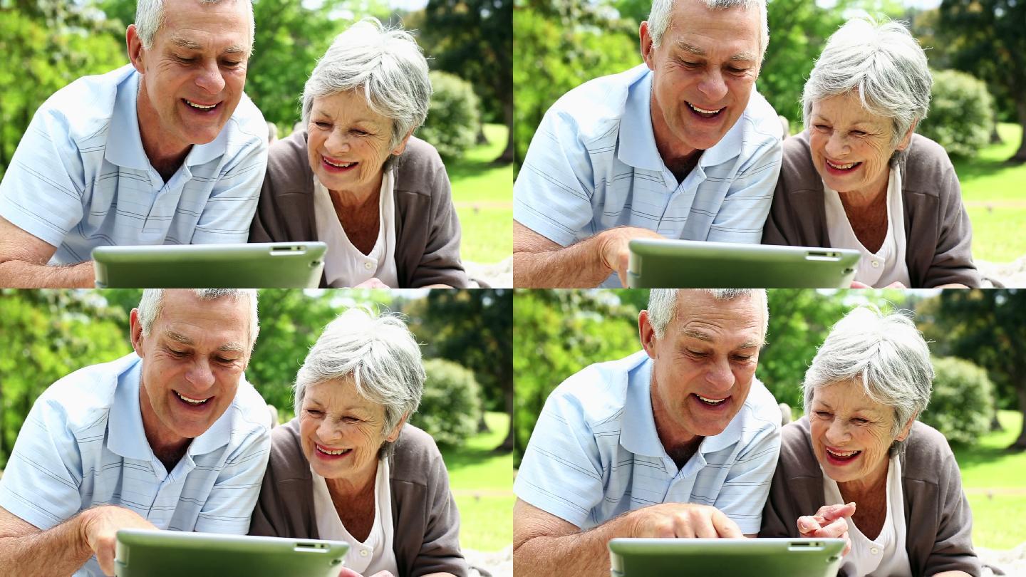 一对快乐的老年夫妇在阳光明媚的日子里用平板电脑在公园里放松
