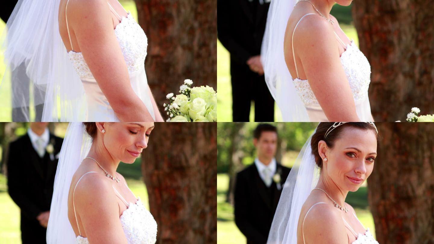 在一个阳光明媚的日子里，新娘对着镜头微笑，而新郎则站在后面