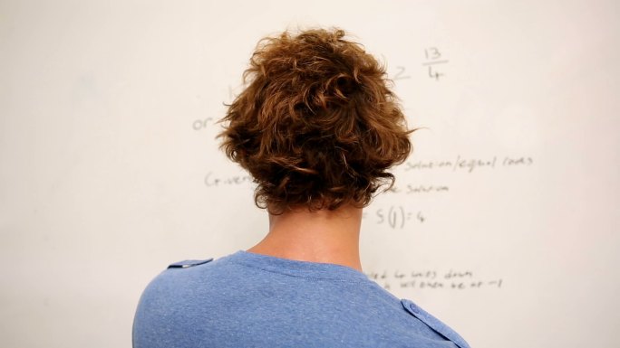 一个困惑的学生站在大学的数学白板前
