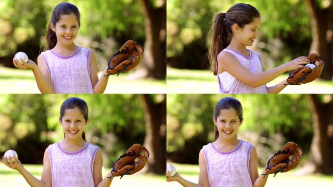 运动小女孩对着镜头微笑，在一个阳光明媚的日子里，在公园里玩棒球