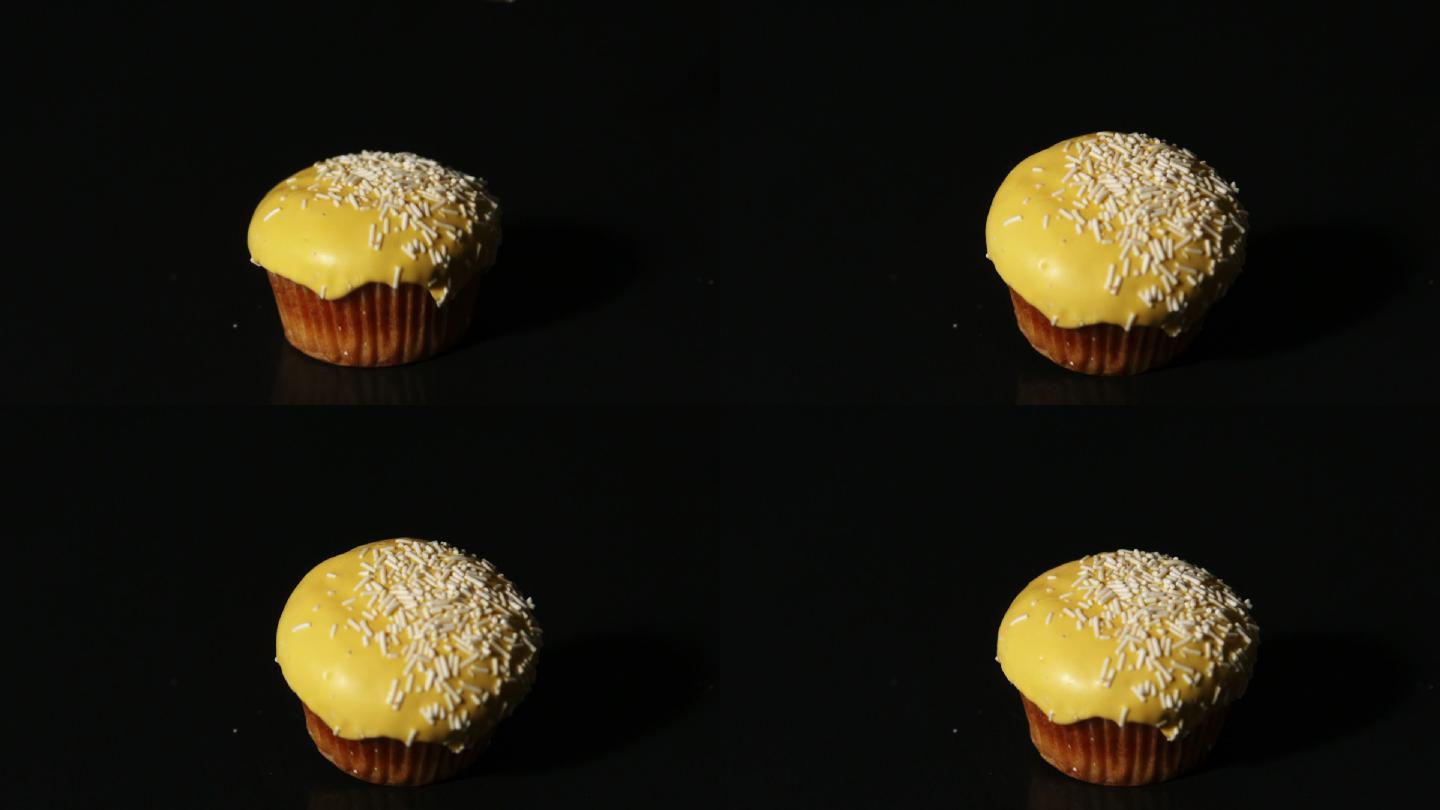 在慢镜头中，黄色的纸杯蛋糕落在黑色背景上
