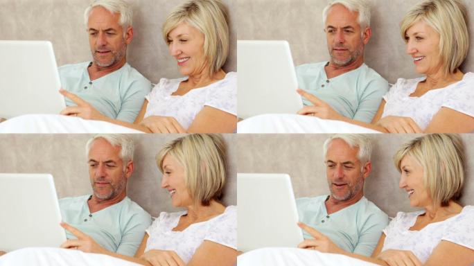 幸福的夫妇聊天和使用笔记本电脑在床上在家里的卧室