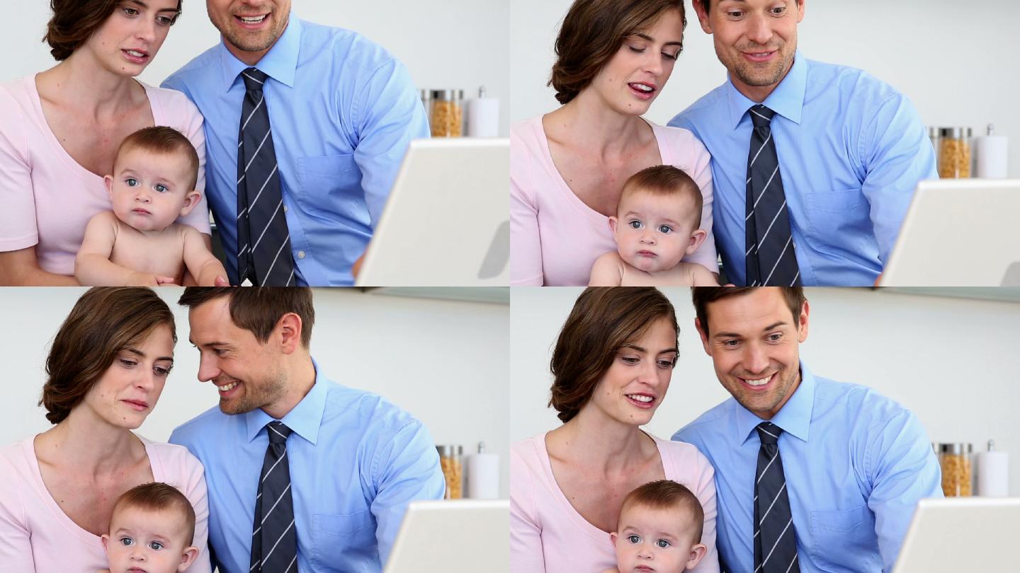 快乐的父母和他们的宝宝在厨房里使用笔记本电脑