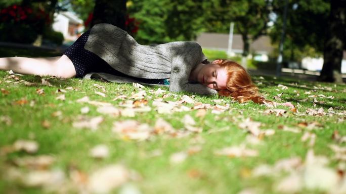 在明亮的阳光下，红头发的人躺在绿色的草坪上安静地打盹
