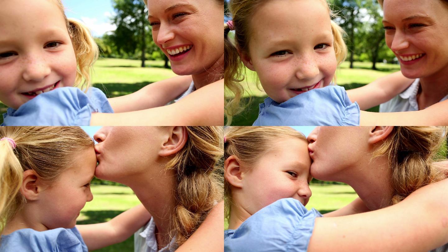 在一个阳光明媚的日子里，快乐的妈妈在公园里亲吻她的小女儿