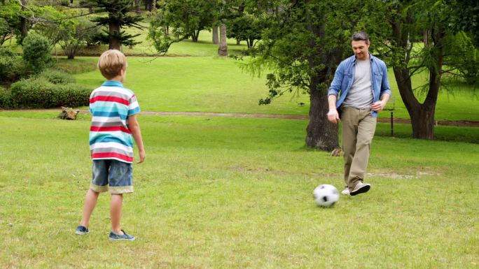 在一个阳光明媚的日子里，父亲和儿子在公园里踢足球