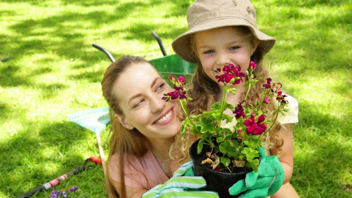 在一个阳光明媚的日子里，一个可爱的小女孩和她的妈妈捧着一盆花