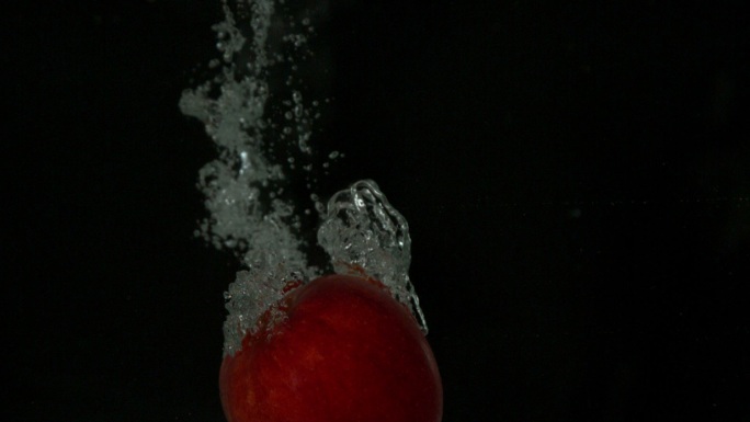 黑色背景下的慢镜头，红苹果坠入水中