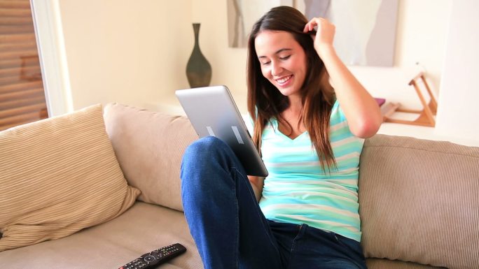 一个漂亮的黑发女孩在客厅的沙发上休息，用着她的平板电脑