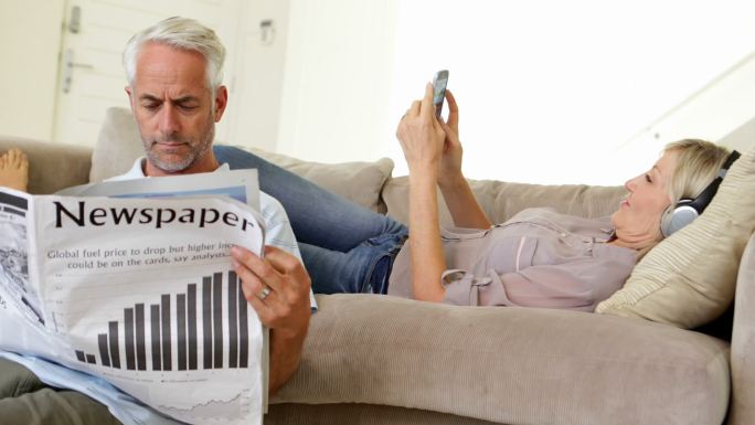 男人在看报纸，而伴侣在客厅的沙发上听音乐