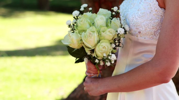 在一个阳光明媚的日子里，新娘手捧花束在公园里