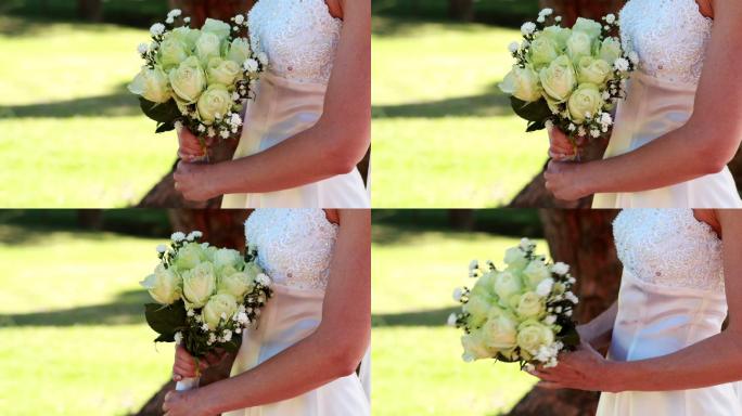 在一个阳光明媚的日子里，新娘手捧花束在公园里