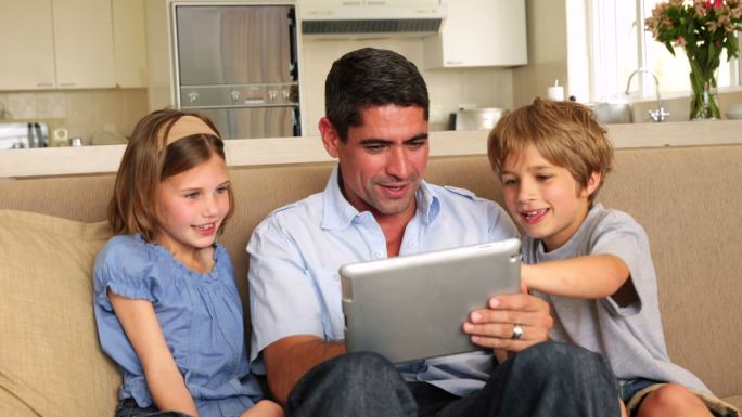 可爱的孩子们在客厅的沙发上和父亲一起使用平板电脑
