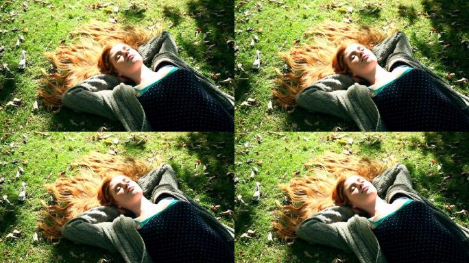 年轻的红发女郎在灿烂的阳光下的草坪上休息