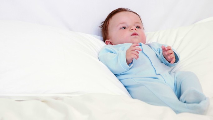 穿着蓝色婴儿草的男婴躺在家里卧室的枕头上