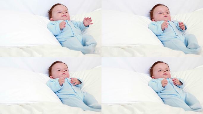 穿着蓝色婴儿草的男婴躺在家里卧室的枕头上