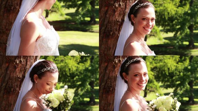 在一个阳光明媚的日子里，美丽的新娘手捧花束在公园里对着镜头微笑