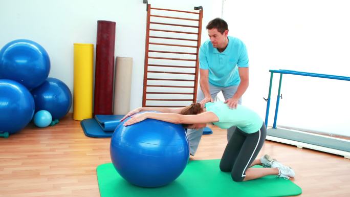 在康复中心，教练帮助他的客户用健身球伸展她的背部