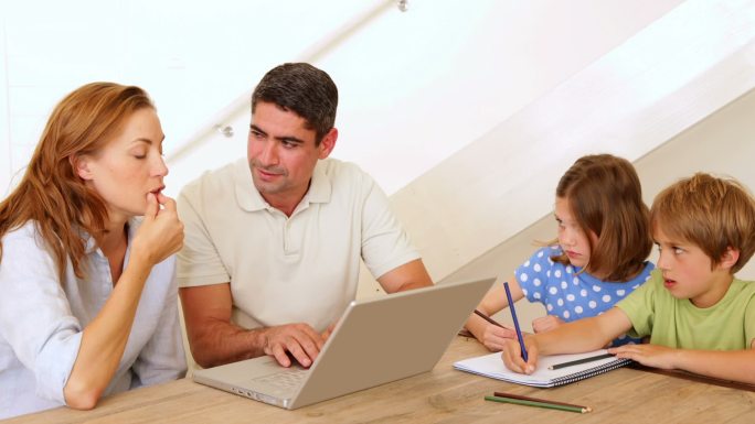 父母使用笔记本电脑，孩子在家里客厅的桌子上上色